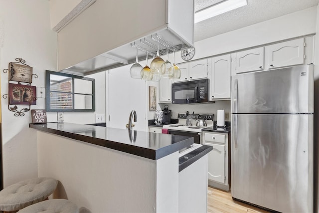 kitchen featuring a peninsula, white electric range oven, dark countertops, freestanding refrigerator, and black microwave