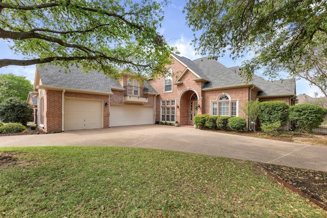 traditional home featuring roof with shingles, driveway, brick siding, an attached garage, and a front yard