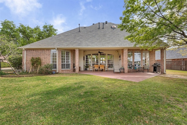 rear view of house featuring fence, ceiling fan, brick siding, and a yard