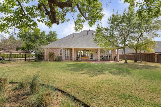 back of house featuring fence, roof with shingles, a patio area, a lawn, and brick siding