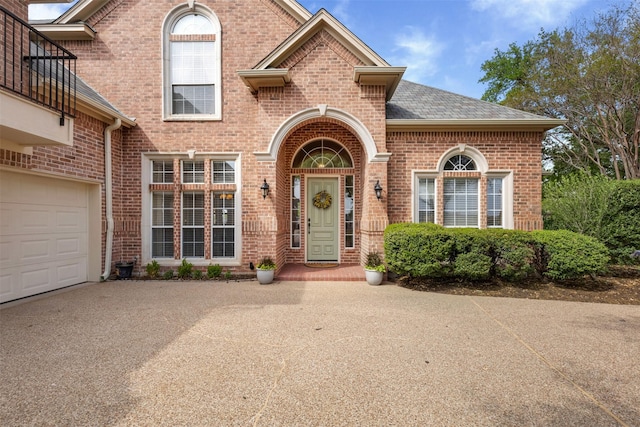 doorway to property featuring brick siding, driveway, a garage, and roof with shingles