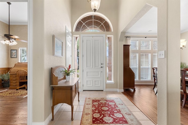 entrance foyer with baseboards, a towering ceiling, a ceiling fan, crown molding, and light tile patterned floors