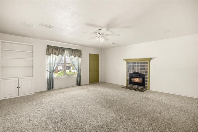 unfurnished living room with a tiled fireplace, visible vents, carpet, baseboards, and a ceiling fan