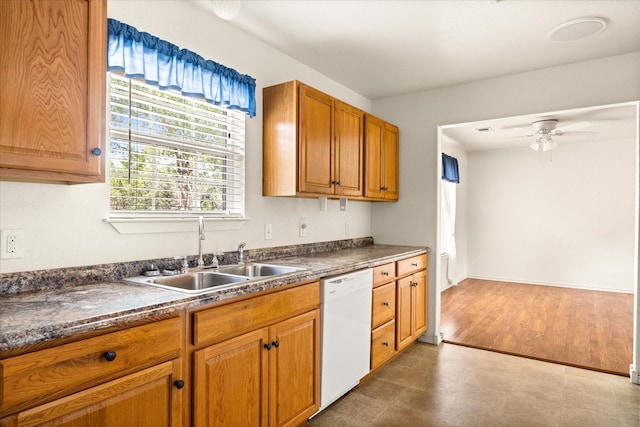 kitchen featuring white dishwasher, dark countertops, a ceiling fan, and a sink