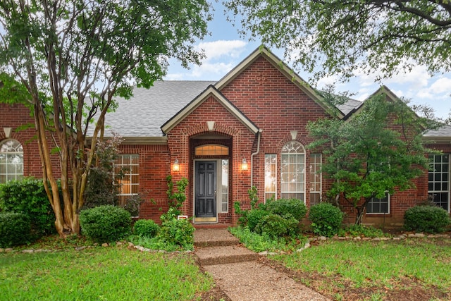 view of front of home featuring brick siding, roof with shingles, and a front yard