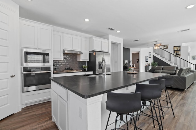 3023 Wind Knot Way, Royse City, TX 75189 - kitchen with stainless steel appliances, dark countertops, dark wood-style flooring, under cabinet range hood, and a center island with sink
