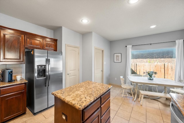 kitchen with light tile patterned flooring, recessed lighting, light stone counters, stainless steel refrigerator with ice dispenser, and a kitchen island