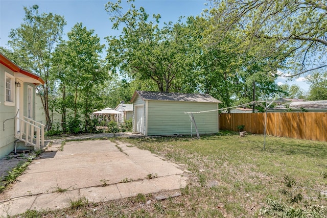 view of yard with concrete driveway, an outdoor structure, fence, and a patio
