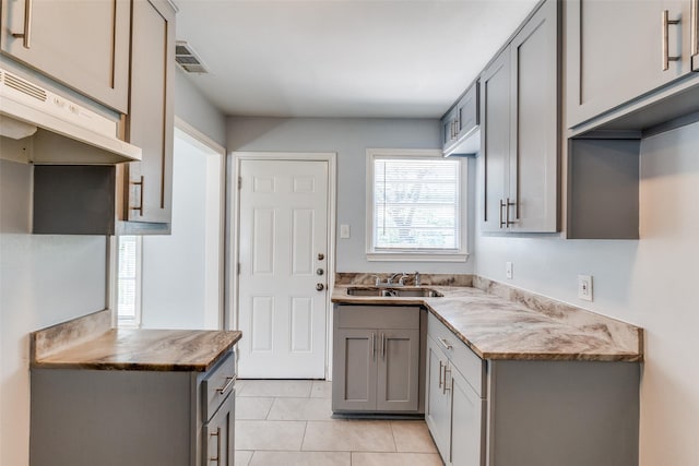 kitchen featuring a sink, visible vents, gray cabinets, under cabinet range hood, and light tile patterned floors