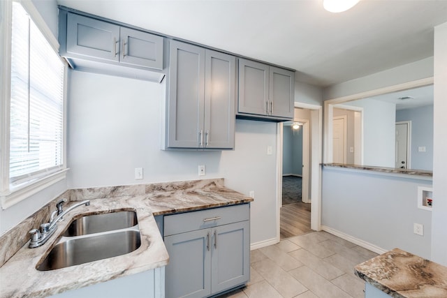 kitchen with visible vents, a sink, light stone countertops, baseboards, and gray cabinetry