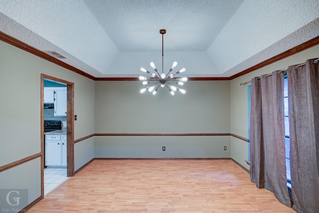 unfurnished room featuring a textured ceiling, light wood-type flooring, an inviting chandelier, a tray ceiling, and visible vents