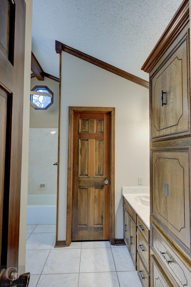 bathroom with tile patterned floors, vaulted ceiling, a bathing tub, vanity, and ornamental molding