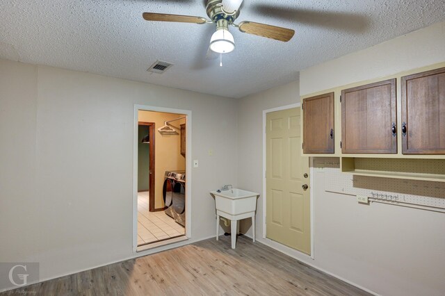 interior space featuring light wood-style flooring, a textured ceiling, visible vents, a ceiling fan, and washer / clothes dryer