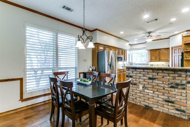 dining space with a textured ceiling, visible vents, hardwood / wood-style flooring, and ceiling fan with notable chandelier