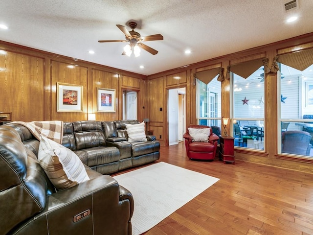 living area featuring ceiling fan, wood walls, wood finished floors, and visible vents