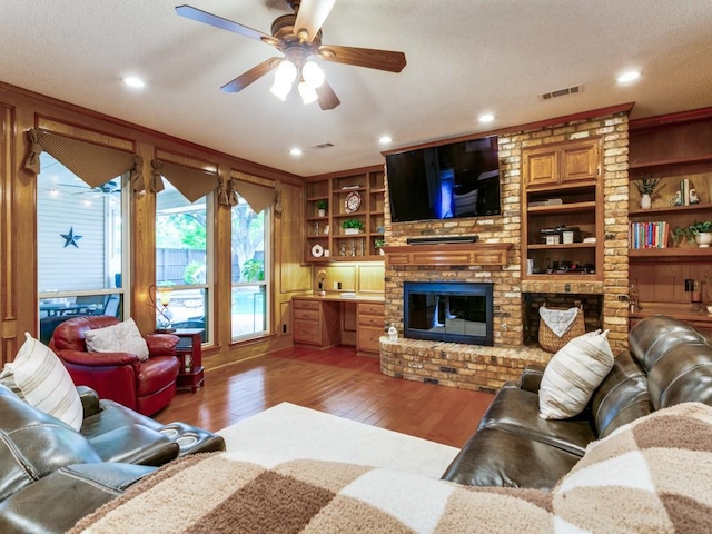 living room with ceiling fan, a textured ceiling, built in features, light wood-style flooring, and visible vents