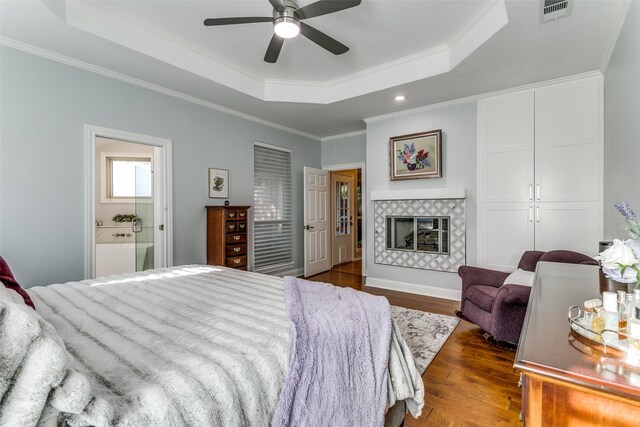 bedroom featuring crown molding, ensuite bathroom, dark wood-type flooring, a tray ceiling, and visible vents