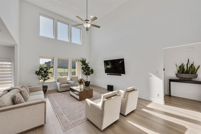 living room with baseboards, a high ceiling, a ceiling fan, and light wood-style flooring
