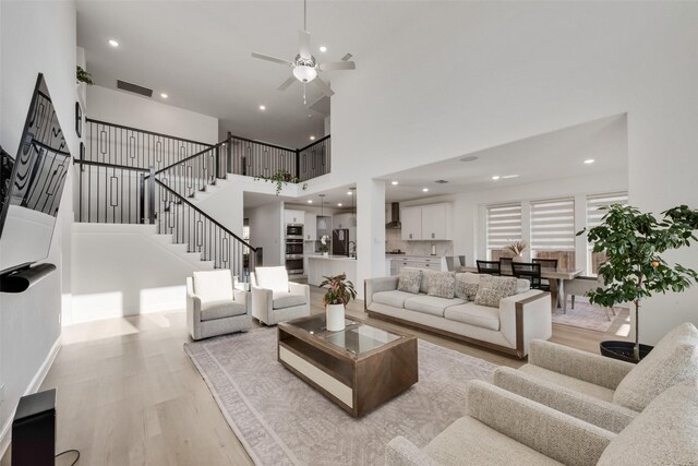 living area with visible vents, recessed lighting, light wood-style floors, a ceiling fan, and a high ceiling