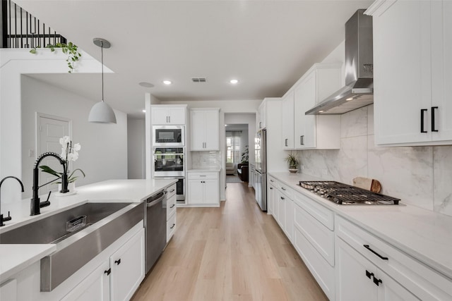 kitchen with stainless steel appliances, a sink, light wood-type flooring, wall chimney exhaust hood, and decorative backsplash