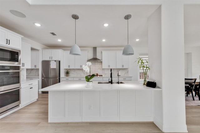 kitchen featuring wall chimney exhaust hood, stainless steel appliances, a sink, decorative backsplash, and light countertops