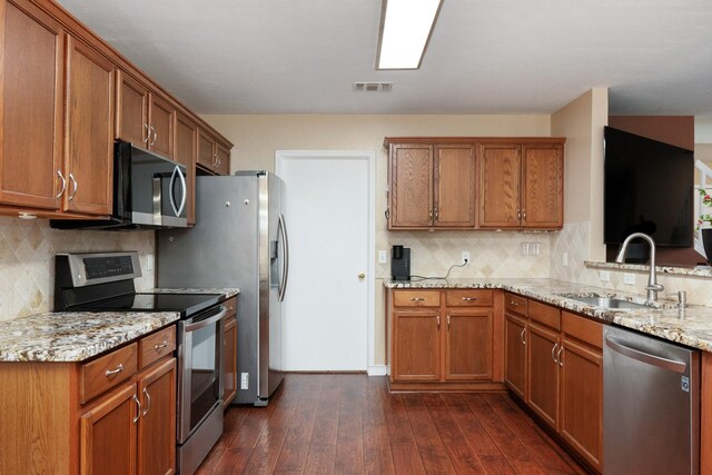 kitchen featuring dark wood-style flooring, appliances with stainless steel finishes, brown cabinetry, and a sink