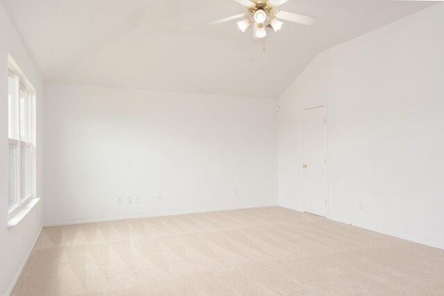 empty room featuring light colored carpet, baseboards, ceiling fan, and vaulted ceiling