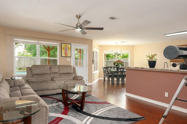 living room with baseboards, ceiling fan with notable chandelier, dark wood finished floors, and visible vents