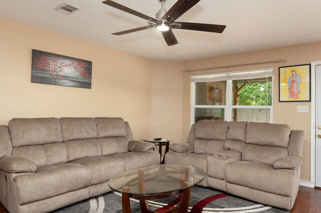 living room with a ceiling fan, visible vents, and dark wood-type flooring