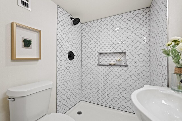 bathroom featuring a tile shower, toilet, a sink, and visible vents