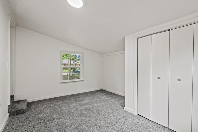 unfurnished bedroom with lofted ceiling, a closet, carpet flooring, and baseboards