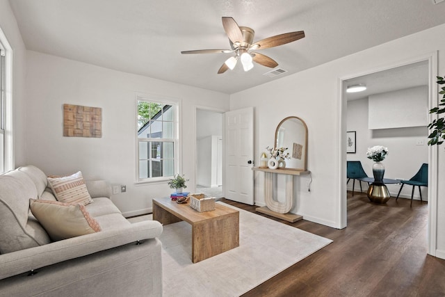 living room with baseboards, visible vents, dark wood-style floors, and ceiling fan