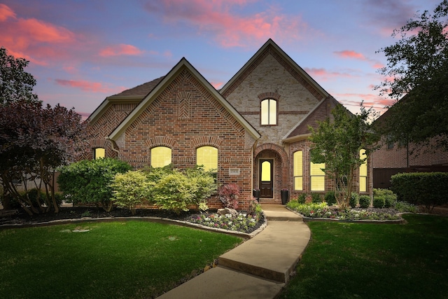 french provincial home with a front yard and brick siding