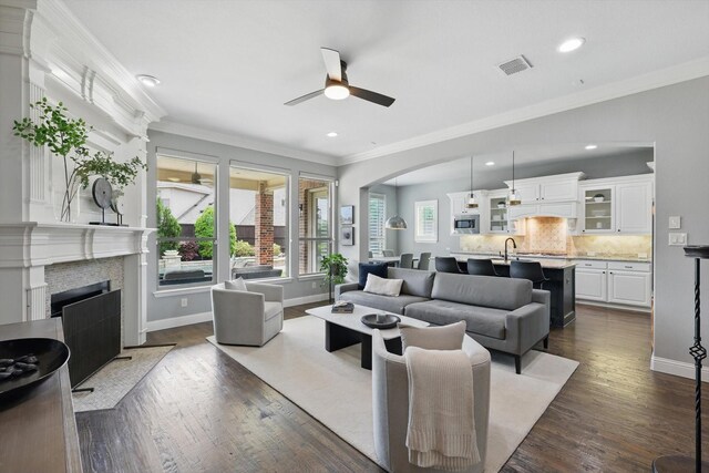 living area with visible vents, ornamental molding, ceiling fan, arched walkways, and a fireplace with flush hearth