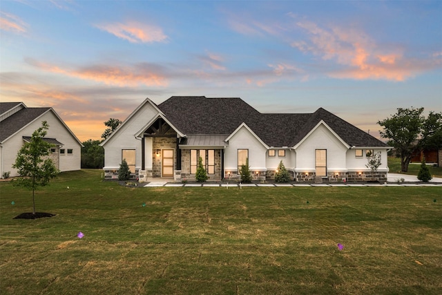 modern farmhouse featuring stone siding, roof with shingles, and a yard