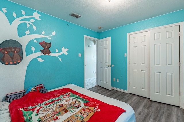 bedroom featuring wood finished floors, visible vents, a closet, baseboards, and a textured ceiling