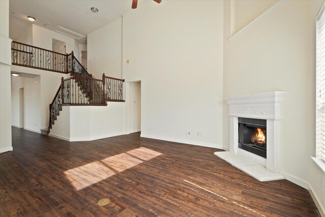 unfurnished living room with stairway, a high ceiling, wood finished floors, baseboards, and a lit fireplace