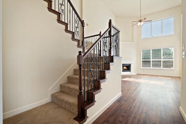 403 Connemara Trl, Celina, TX 75009 - staircase featuring a ceiling fan, baseboards, wood finished floors, a towering ceiling, and a warm lit fireplace