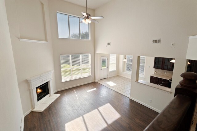 unfurnished living room featuring a high end fireplace, wood finished floors, visible vents, and a towering ceiling