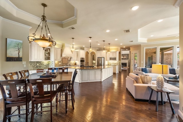 dining space with dark wood finished floors, crown molding, visible vents, and a raised ceiling