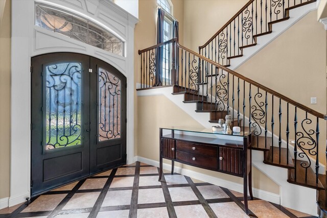 foyer entrance with a towering ceiling, french doors, baseboards, and stairs