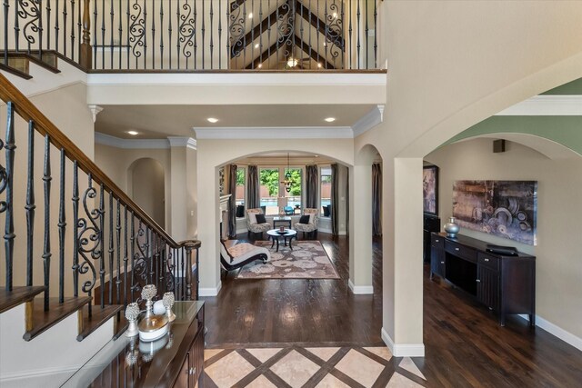 entryway with arched walkways, wood finished floors, baseboards, a high ceiling, and crown molding