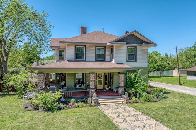view of front of house with a chimney, fence, covered porch, roof with shingles, and a front yard