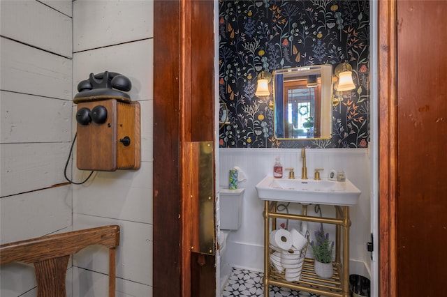 bathroom with a wainscoted wall, a sink, and wallpapered walls