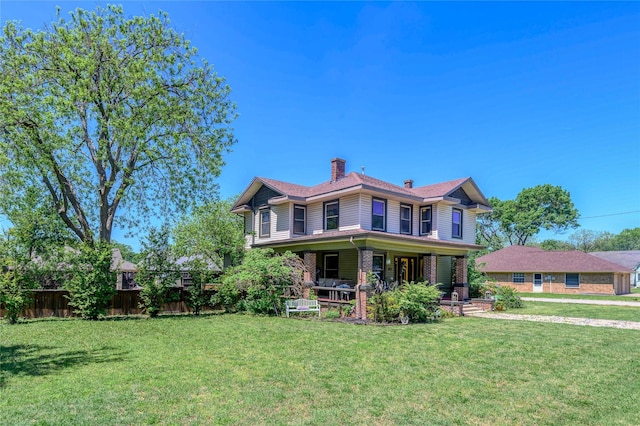 victorian home with a porch, a chimney, fence, and a front yard
