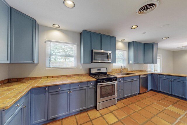 kitchen featuring a sink, tile countertops, blue cabinetry, appliances with stainless steel finishes, and visible vents