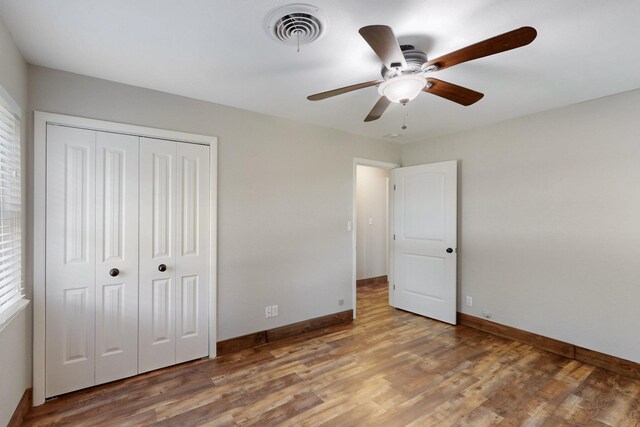 unfurnished bedroom featuring baseboards, visible vents, wood finished floors, a closet, and ceiling fan