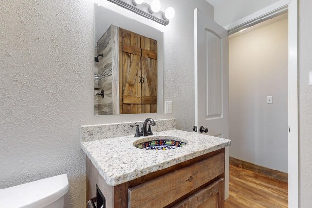 bathroom with wood finished floors, a textured wall, toilet, vanity, and a shower