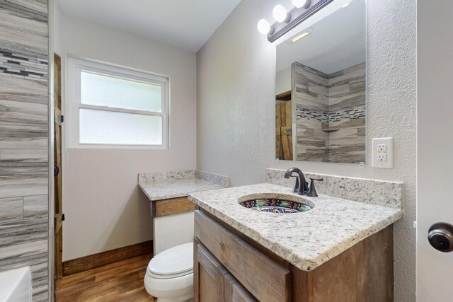 bathroom with wood finished floors, a textured wall, toilet, vanity, and baseboards