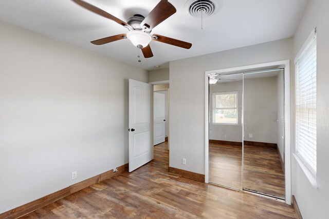 unfurnished bedroom featuring wood finished floors, visible vents, a ceiling fan, a closet, and baseboards